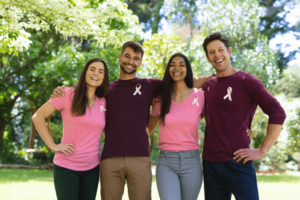four young adults standing in a line with breast cancer awareness ribbons on